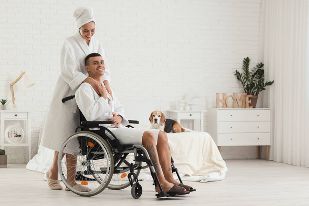 Молодий чоловік в інвалідному візку і його дружина після душу з собакою Бігль вдома - Фото, зображення