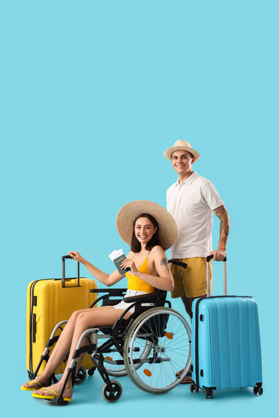 青い背景のスーツケースと車椅子にいる若い男と彼の妻 - 写真・画像