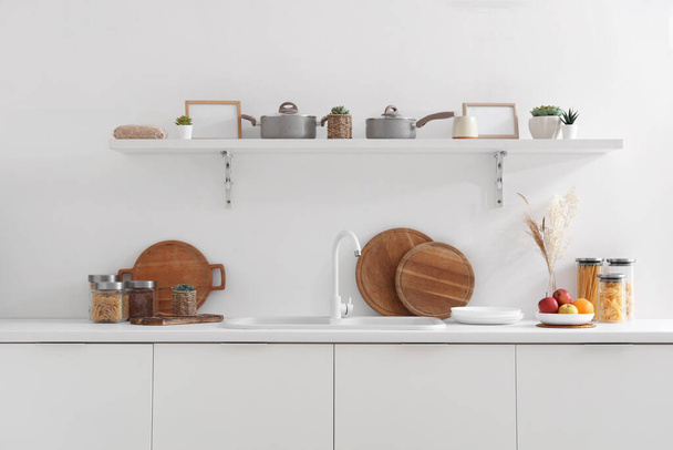 Modern konyha belseje fehér pulttal, polccal, mosogatóval és evőeszközökkel - Fotó, kép