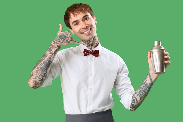 Jonge barman met shaker met "call me" gebaar op groene achtergrond - Foto, afbeelding