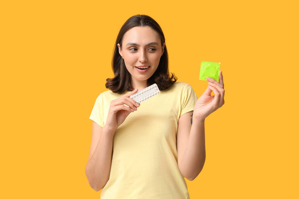 黄色の背景にコンドームと出産制御薬を有する美しい若い女性. 安全なセックスコンセプト - 写真・画像