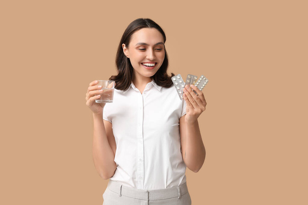 Krásná mladá žena s antikoncepci pilulky a sklenice vody na hnědém pozadí. Bezpečný sexuální koncept - Fotografie, Obrázek