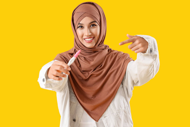 Gyönyörű muszlim nő rámutatva terhességi teszt sárga alapon - Fotó, kép