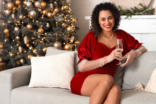 Mooie Afro-Amerikaanse vrouw met glas champagne vieren Nieuwjaar thuis - Foto, afbeelding