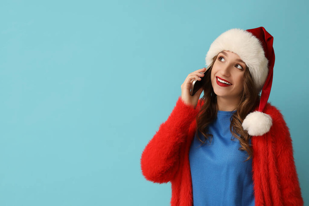 Jovem mulher em Santa chapéu falando por telefone celular no fundo azul - Foto, Imagem