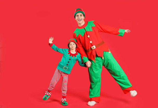 Père et son mignon petit fils en costumes d'elfe s'amusent sur fond rouge - Photo, image