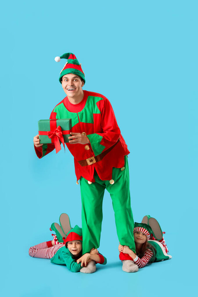Pai e crianças bonitos em trajes de elfo com caixa de presente no fundo azul - Foto, Imagem