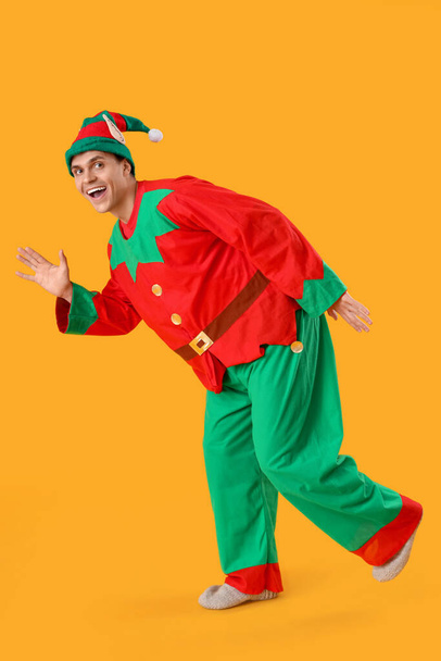 Handsome young man in elf's costume waving hand on yellow background - Photo, Image