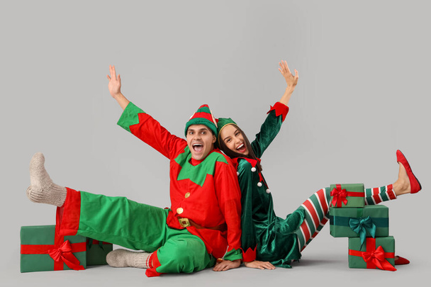 Gelukkig paar in elf kostuums met geschenkdozen zitten op grijze achtergrond - Foto, afbeelding