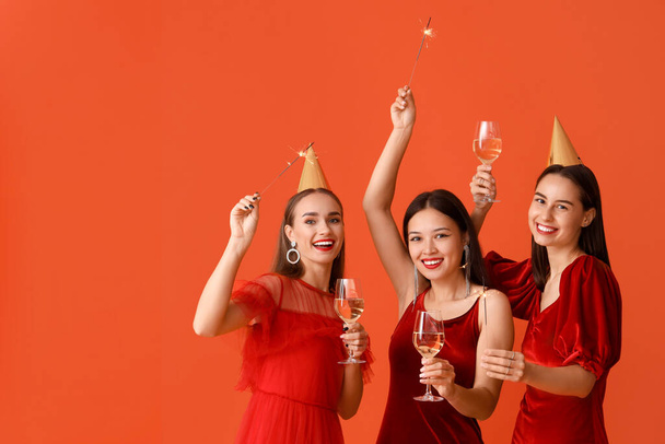 Krásné mladé ženy se šampaňským a jiskry na oranžovém pozadí. Novoroční oslava - Fotografie, Obrázek