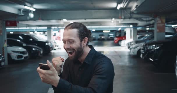 Κοιτάζει το κινητό του και δεν μπορεί να πιστέψει την ευτυχία του. Η Millennial είναι ευχαριστημένη επειδή έλαβε ένα χαρούμενο μήνυμα για μια μεγάλη νίκη. Μεγάλο χαρούμενο γεγονός πιάστηκε άνθρωπος ακριβώς στο υπόγειο πάρκινγκ. - Πλάνα, βίντεο