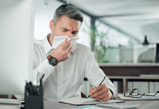 Business man blowing nose at desk in office for allergies, cold and sick virus while writing in notebook. Mature entrepreneur with tissue for infection, influenza or allergy risk while planning notes. - Photo, Image