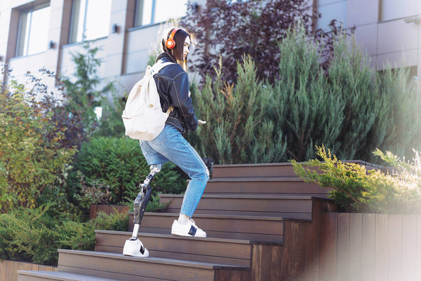 Een jonge studente met een kunstbeen die boven in de stad loopt. Gehandicapte vrouw met een kunstbeen via een trap. Vrouw met been prothese apparatuur. - Foto, afbeelding