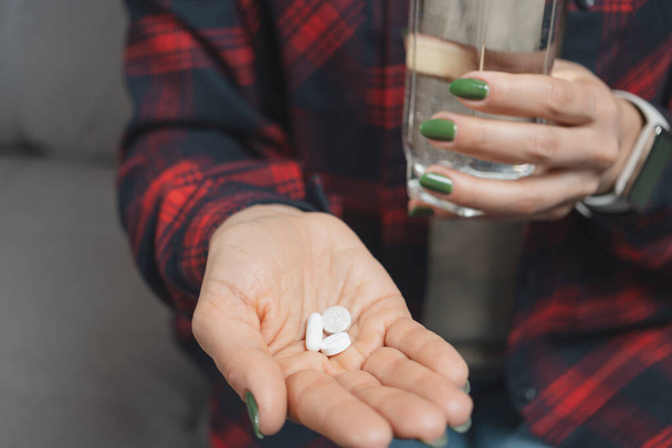 Young woman takes a medicine, holds in a hand white pills and glass of water, close-up view. - Photo, Image