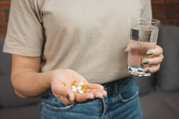 Mulher jovem detém várias pílulas médicas e cápsulas em uma mão e vidro de água, vista de close-up. - Foto, Imagem