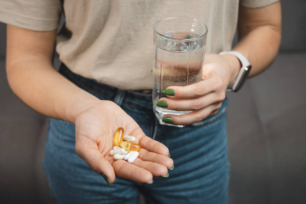 Mujer joven sostiene varias píldoras y cápsulas médicas en una mano y un vaso de agua, vista de cerca. - Foto, Imagen