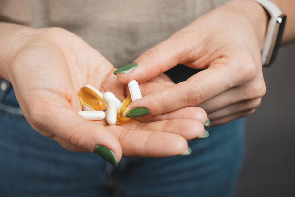 Fiatal nő vesz egy fehér orvosi tablettát, és tartja a kézi halom különböző tabletták és kapszulák, közelkép. - Fotó, kép