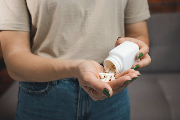Mujer joven sostiene cápsulas médicas blancas y pastillas en una mano, tomar medicamentos de un frasco, vista de cerca. - Foto, imagen