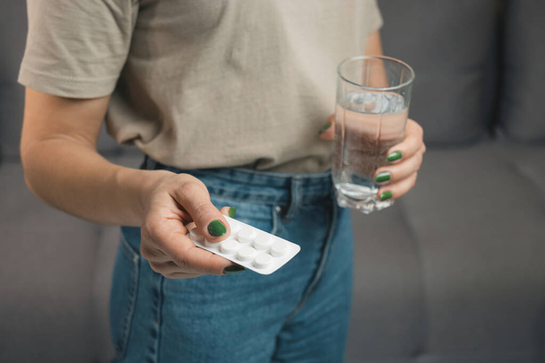 Young woman holds a medicine, blister pack with pills for treatment and glass of water, close-up view. - Photo, Image