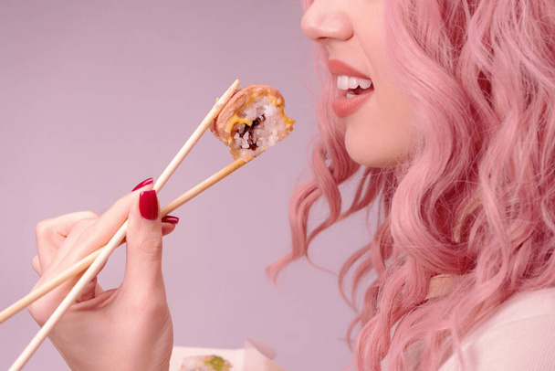 Young woman with red nails and pink hair is eating sushi close up. - Photo, Image