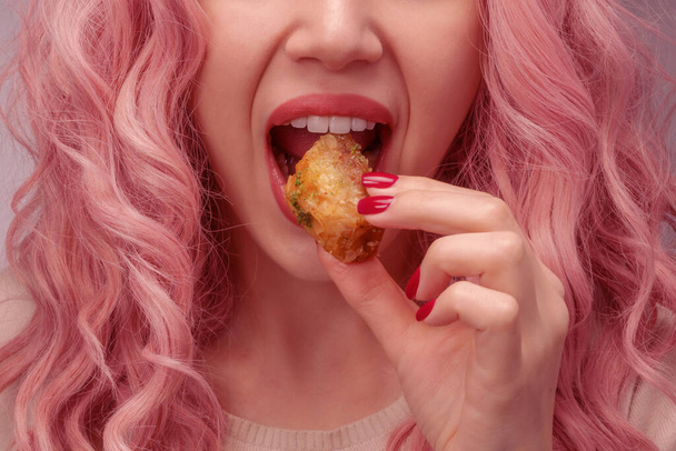 Nő rózsaszín göndör haj eszik baklava közelkép. - Fotó, kép