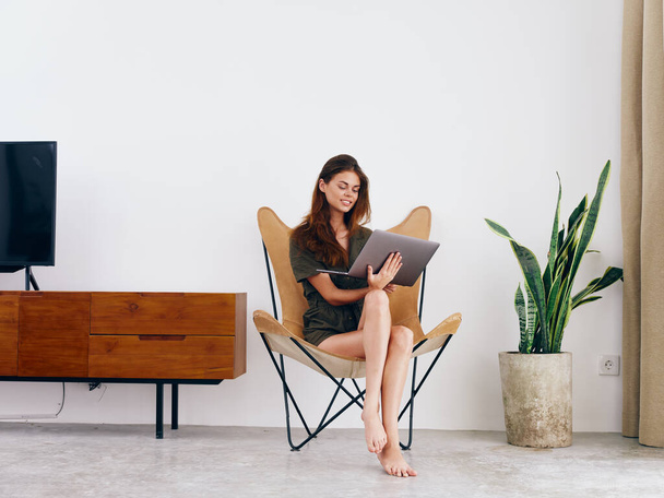 Studentka siedzi na krześle z laptopem w domu uśmiech i relaks, nowoczesne stylowe wnętrze skandynawskiego stylu życia, przestrzeń do kopiowania. Wysokiej jakości zdjęcie - Zdjęcie, obraz
