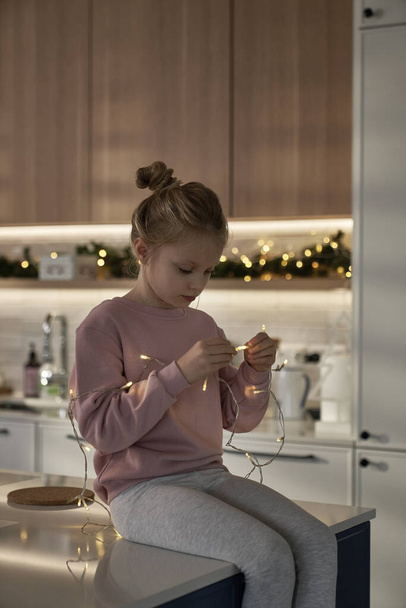 Kaukasische Mädchen spielen mit Weihnachtsbeleuchtung in der Küche - Foto, Bild