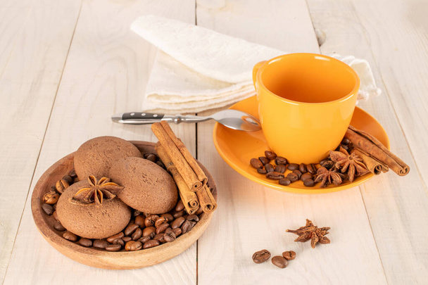Schokoladenkekse, Zimt, Sternanis, Kaffeebohnen auf einem Keramikteller mit einer Tasse auf einem Holztisch. - Foto, Bild
