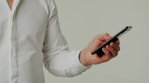 Αριστερό χέρι κύλιση γρήγορα smartphone. Επιχειρηματίας σε λευκό πουκάμισο περιήγηση social media απομονώνονται σε γκρι φόντο χρώμα. Στέλνει sms στο συνεργάτη του με ραντεβού. Έλεγχος εισερχόμενων μηνυμάτων από εργαζόμενο - Πλάνα, βίντεο