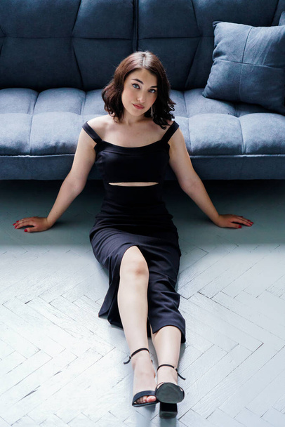 Young beautiful girl in a black dress sitting on the sofa - Foto, Bild