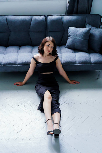 Young beautiful girl in a black dress sitting on the sofa - Фото, зображення