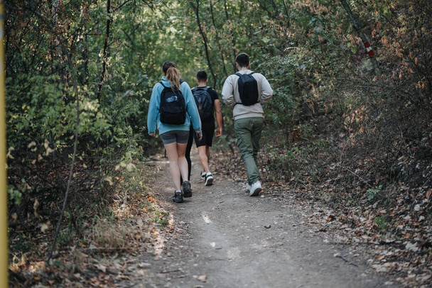 Sportfreunde wandern und genießen einen sonnigen Tag in einem malerischen Herbstwald. Sie diskutieren Themen und haben Spaß, während sie die natürliche Umgebung erkunden und sich körperlich betätigen.. - Foto, Bild
