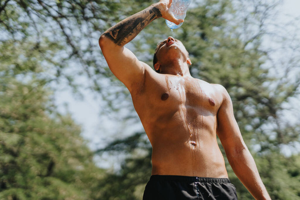 Caucasian athlete, in sportswear, actively exercising outdoors. Fit body, strong muscles, and motivation. Refreshing break, drinking water, enjoying the sunny day. - Photo, Image