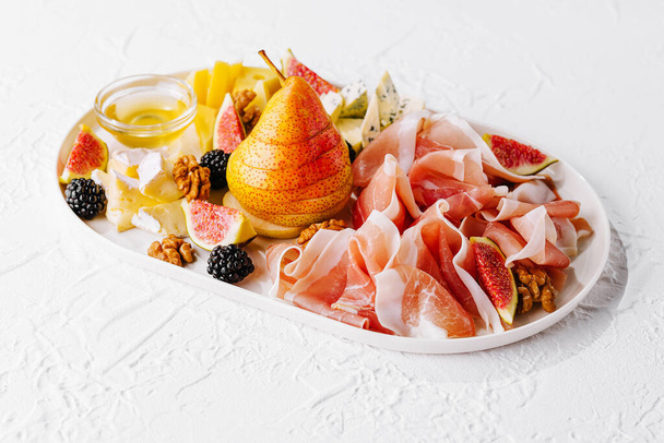 Italiaanse antipasto met prosciutto, kaas, noten en fruit - Foto, afbeelding