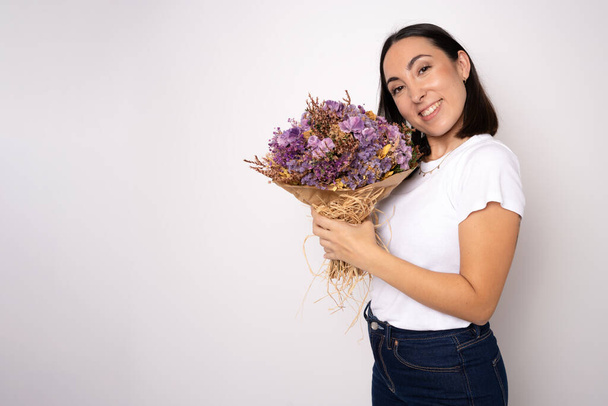 Portrait of a delighted young woman in casual clothes holding big bouquet of flowers isolated over white background - Photo, Image