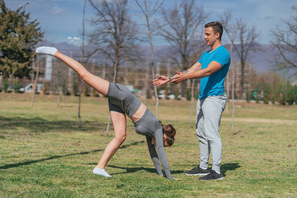 Kollarının üzerinde durmaya çalışan esmer bir sporcu kız resmi. Erkek arkadaşı ona yardım ediyor. - Fotoğraf, Görsel