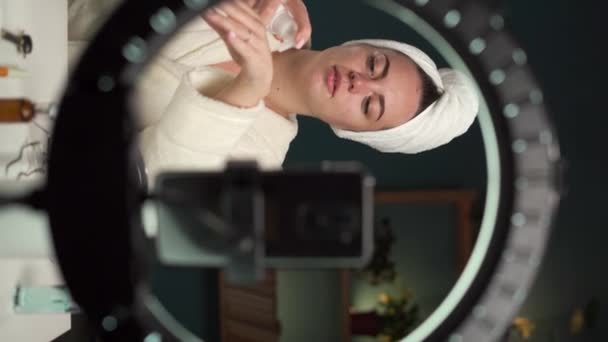 Vrouwelijke blogger het aanbrengen van handcrème op haar handen tijdens het vloggen op smartphone thuis. - Video