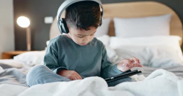 Мальчик, малыш и планшет с наушниками в спальне для онлайн-игр, просмотра фильмов и игры в образовательное приложение по ночам. Дети, цифровые технологии и прослушивание мультимедиа, музыки и потоковых мультфильмов. - Кадры, видео
