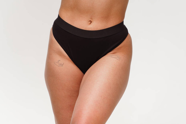 Een vrouw met een mooie vrouwelijke figuur in zwarte lingerie met overgewicht, cellulitis en striae. Obesitas, hormonen en gezondheid. Geïsoleerd op een witte achtergrond. - Foto, afbeelding