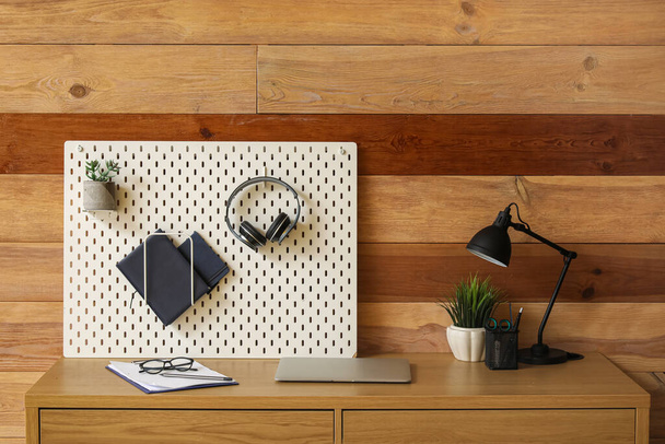 Moderner Arbeitsplatz mit Steckbrett nahe Holzwand im Büro - Foto, Bild