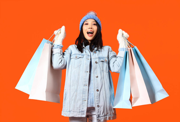 Joven mujer asiática en ropa de invierno con bolsas de compras sobre fondo naranja - Foto, imagen