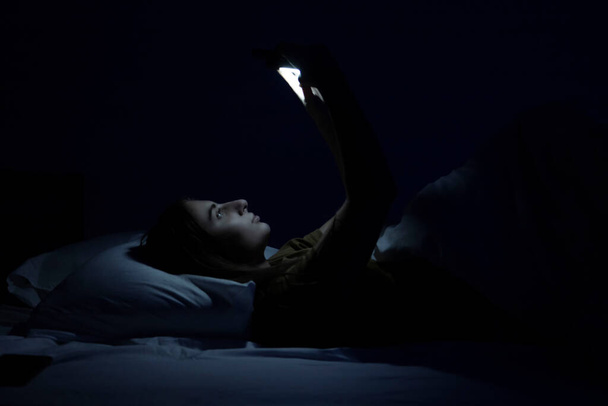gyönyörű fiatal lány az ágyban fehér ágy és telefon. - Fotó, kép