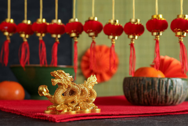 Праздничная композиция с фигуркой золотого дракона, традиционным китайским декором и мандаринами на черном столе. Новогодний праздник - Фото, изображение