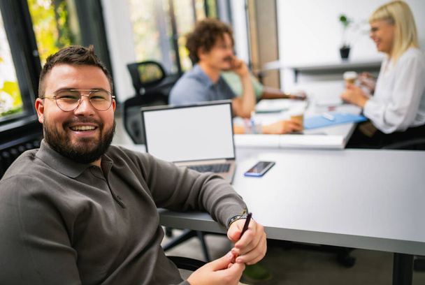 Erkek Çalışan Ofiste Gülümsüyor, Meslektaşları Arkaplanda. - Fotoğraf, Görsel