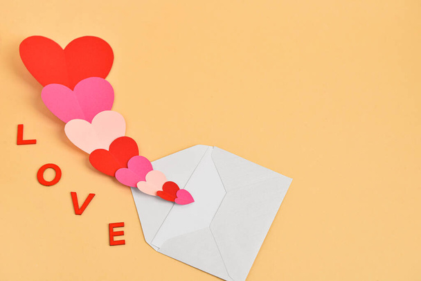Word LOVE with different paper hearts and envelope on yellow background - Photo, Image