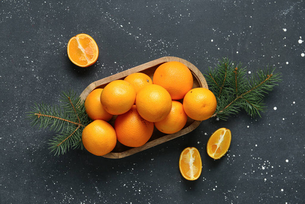 Drewniana deska ze smacznymi pomarańczami i gałązkami jodły na czarnym tle - Zdjęcie, obraz