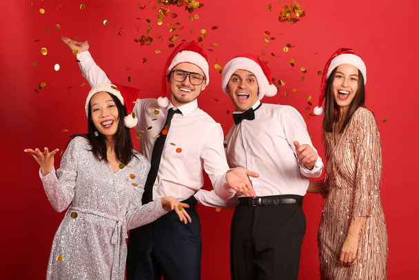 Grupo de amigos con confeti sobre fondo rojo. Celebración de Año Nuevo - Foto, Imagen