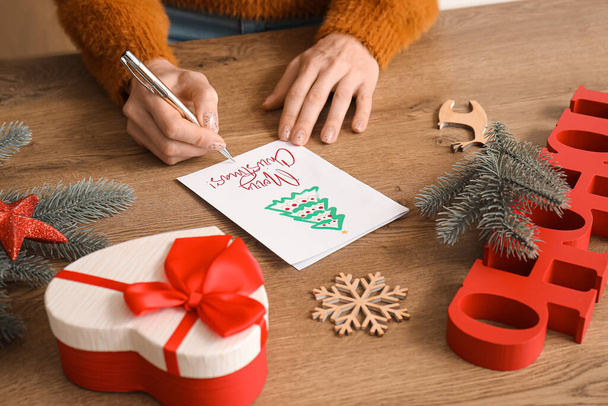 Ώριμη γυναίκα που γράφει ευχετήρια κάρτα για τη γιορτή των Χριστουγέννων στο τραπέζι, κοντινό πλάνο - Φωτογραφία, εικόνα