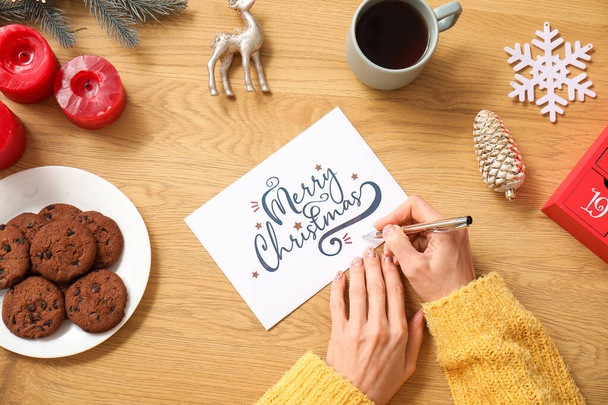 Mature woman writing greeting card for Christmas celebration on wooden table, top view - Photo, Image