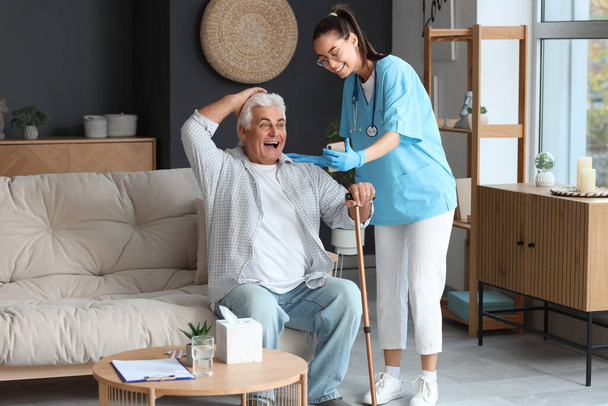 Verpleegster toont mobiele telefoon aan senior man met stok thuis - Foto, afbeelding